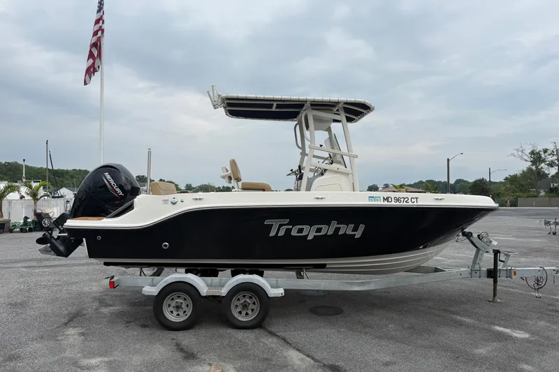 The Image of 2022 Bayliner Trophy T20CX boat on trailer, parked outdoors with American flag in background. - 0