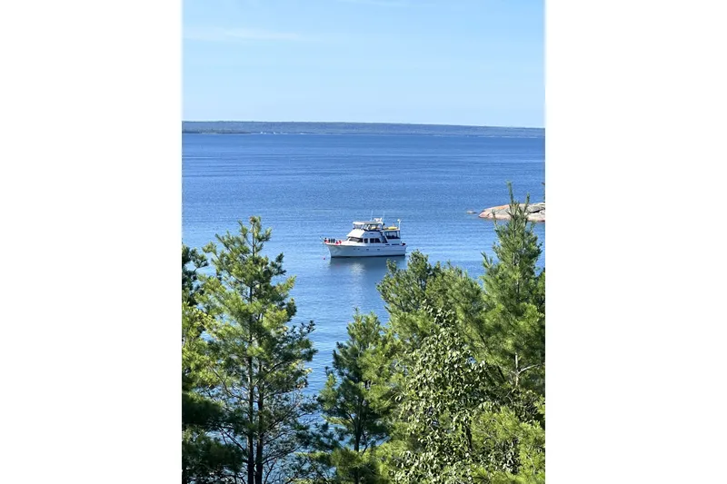 Slide: The Image of A 1985 Jefferson boat anchored on a serene blue lake, surrounded by lush green trees. - 92