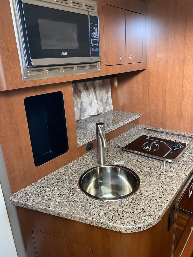 Slide: The Image of The 2023 Crownline 310 CRX galley features a granite countertop, round sink, and microwave. - 21