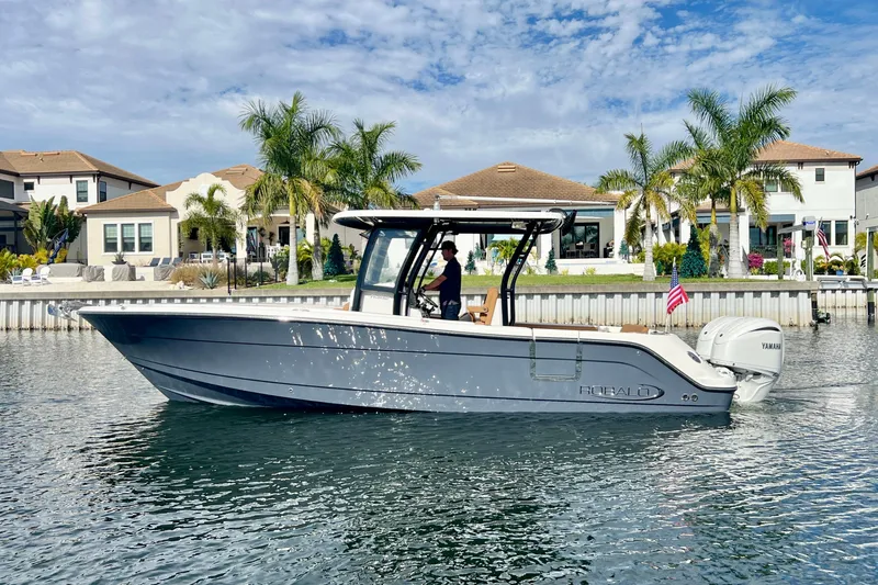 Slide: The Image of 2025 Robalo R302 Center Console boat on water, with waterfront homes and palm trees in background. - 3