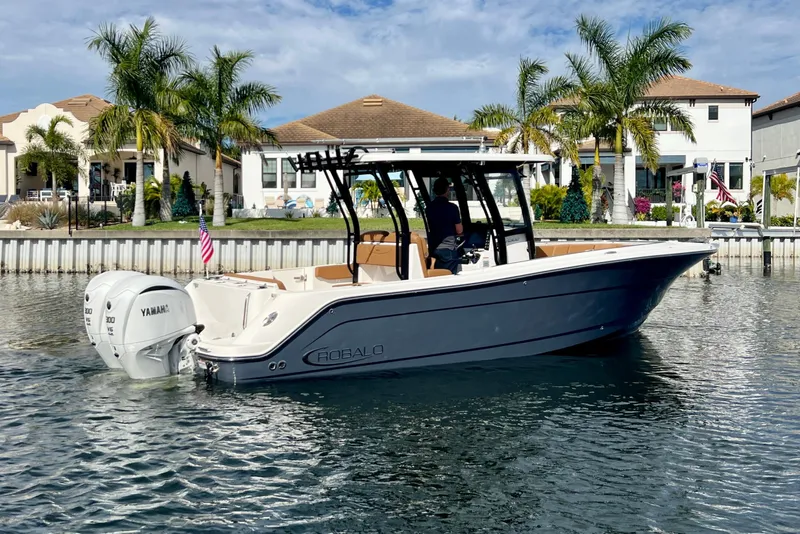 Slide: The Image of 2025 Robalo R302 Center Console boat on water, with palm trees and houses in the background. - 7