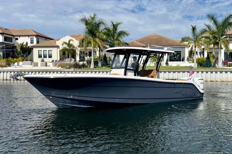The Image of 2025 Robalo R302 Center Console boat on water, with waterfront homes and palm trees in background. - 0