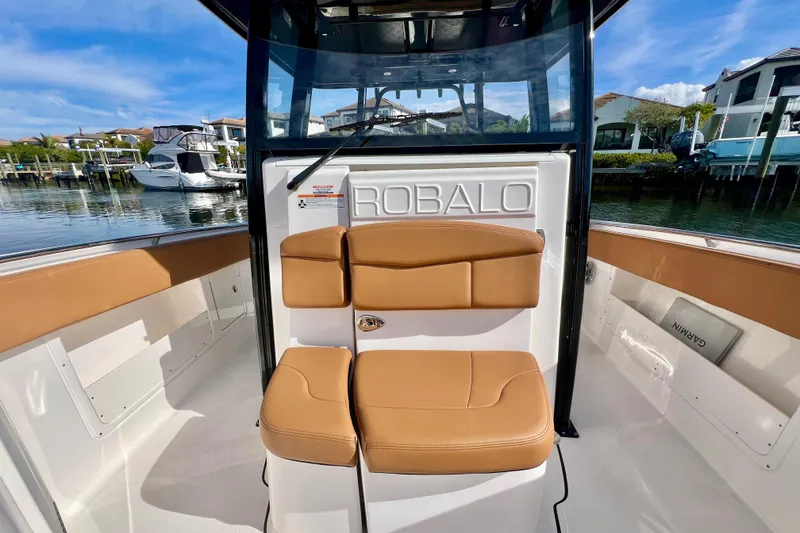 Slide: The Image of 2025 Robalo R302 Center Console boat interior with tan seating, docked by waterfront homes. - 22