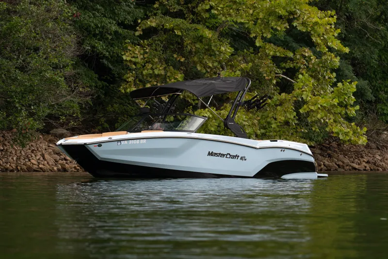 The Image of 2026 MasterCraft NXT23 boat on a calm lake, surrounded by lush greenery. - 1