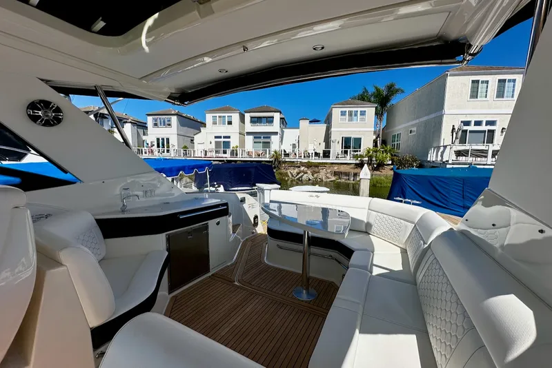 Slide: The Image of The image shows the cockpit of a 2021 Sea Ray Sundancer 320 Outboard. It features white upholstery and a table, overlooking modern waterfront homes. - 21
