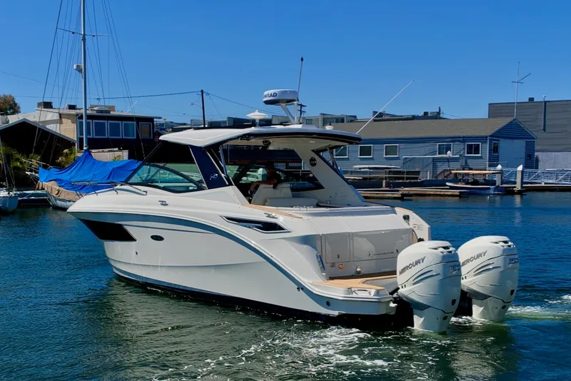 Slide: The Image of A 2021 Sea Ray Sundancer 320 Outboard cruising on calm water. It features twin outboard engines. - 6
