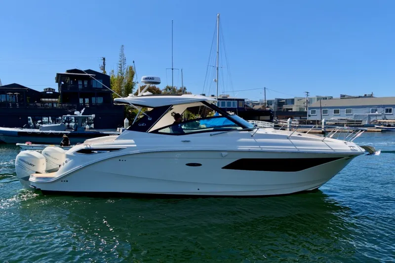 Slide: The Image of The 2021 Sea Ray Sundancer 320 Outboard glides elegantly through the water, surrounded by modern buildings. - 11