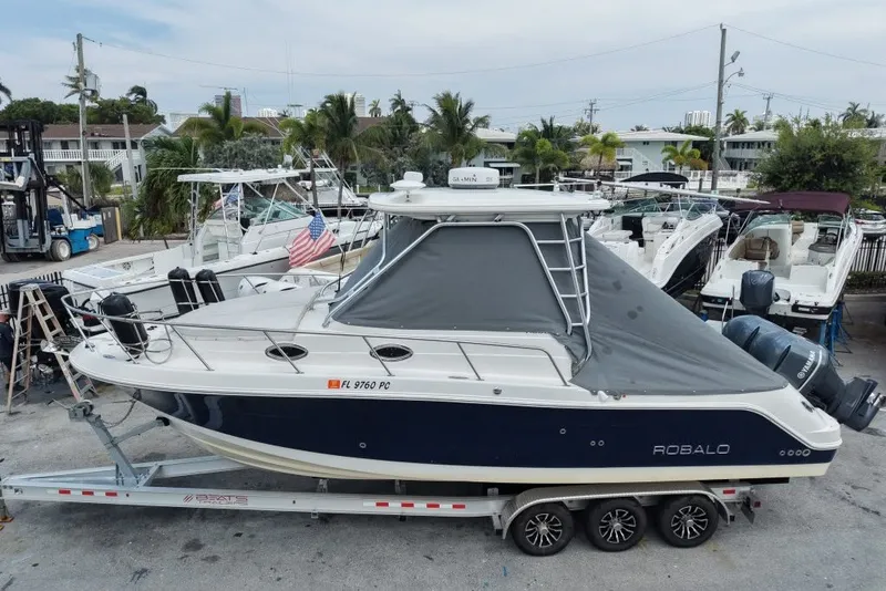 Slide: The Image of 2011 Robalo R305 Walkaround boat on trailer, parked in marina with other boats. - 2