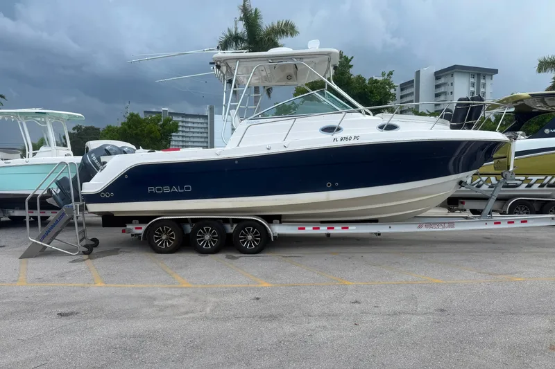 Slide: The Image of 2011 Robalo R305 Walkaround boat on trailer, parked in a lot with cloudy sky. - 11
