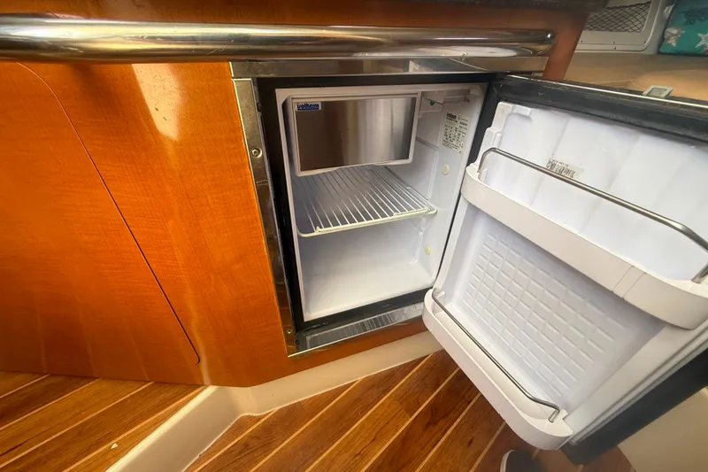 Slide: The Image of 2011 Robalo R305 Walkaround boat interior with open mini fridge, wooden cabinetry, and flooring. - 44