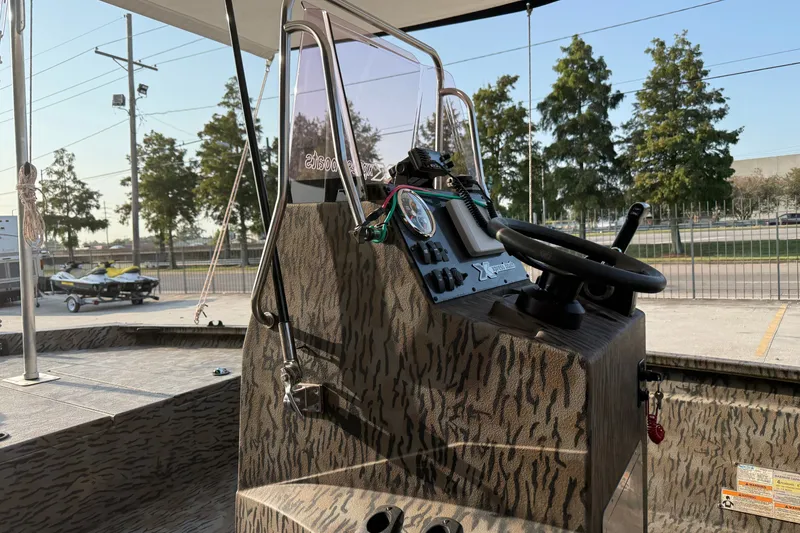 Slide: The Image of 2024 Xpress H190B Bay boat console with steering wheel and controls, featuring a camo design. - 13