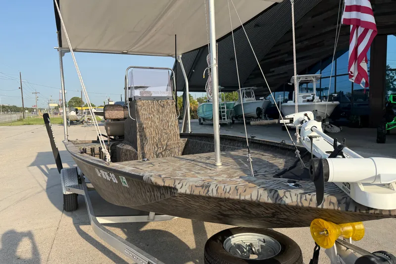 Slide: The Image of 2024 Xpress H190B Bay boat with camouflage design, parked on a trailer under a canopy. - 5