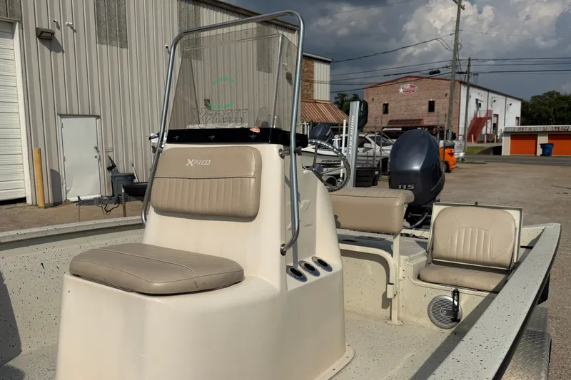 Slide: The Image of 2013 Xpress H20B Bay boat with beige seating, parked outdoors near industrial buildings. - 17