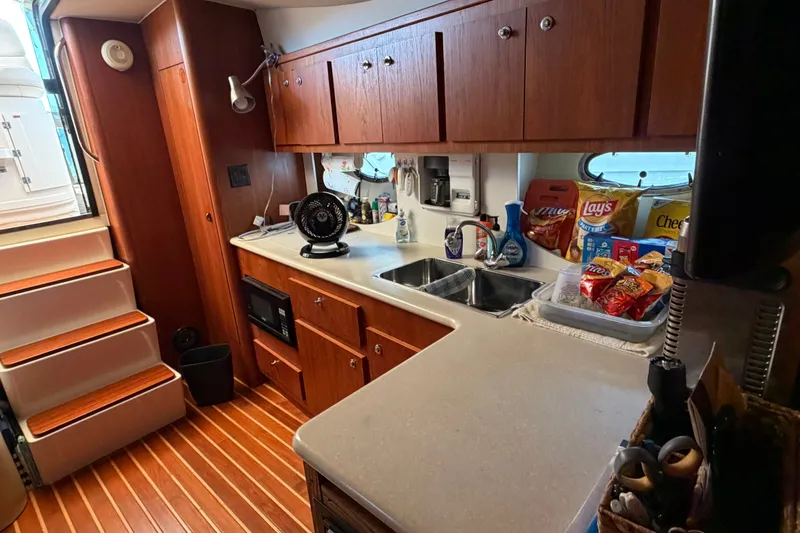 Slide: The Image of Compact kitchen area in a 2001 Tiara 35 Express boat, featuring wooden cabinets and snacks. - 16