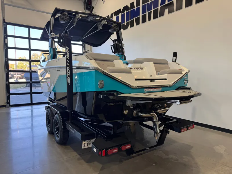 Slide: The Image of A 2024 Super Air Nautique G23 in a showroom. It features a turquoise stern and a trailer. - 6