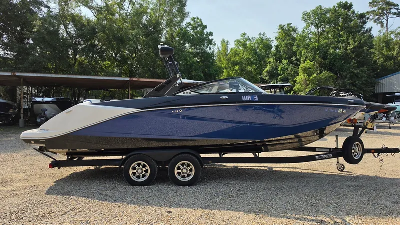 Slide: The Image of A blue and white 2019 Scarab 255 ID Wake Edition boat on a trailer in a gravel lot. - 5