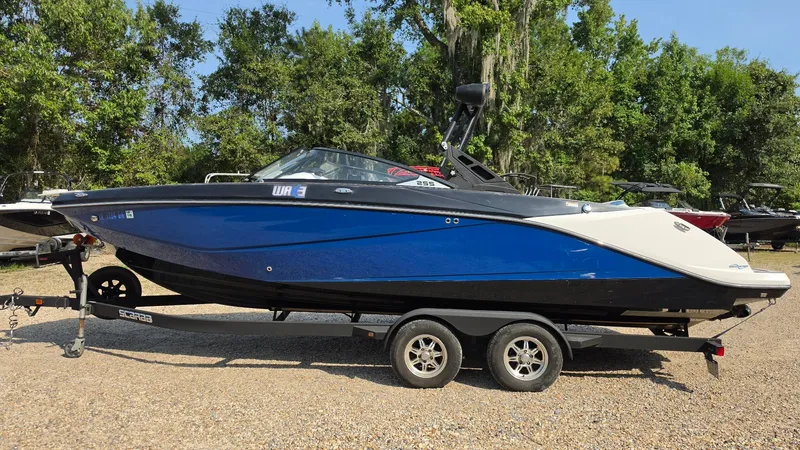 Slide: The Image of A blue and white 2019 Scarab 255 ID Wake Edition boat on a trailer outdoors. - 2