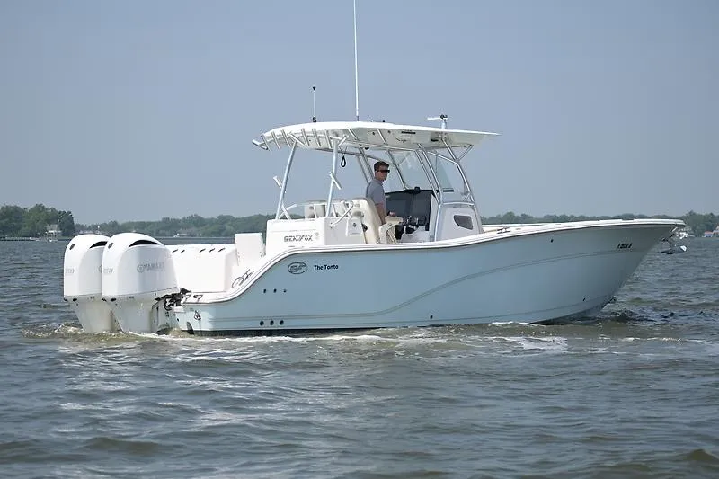 The Image of A white boat cruising on calm water, featuring two outboard engines and a covered helm area. - 0
