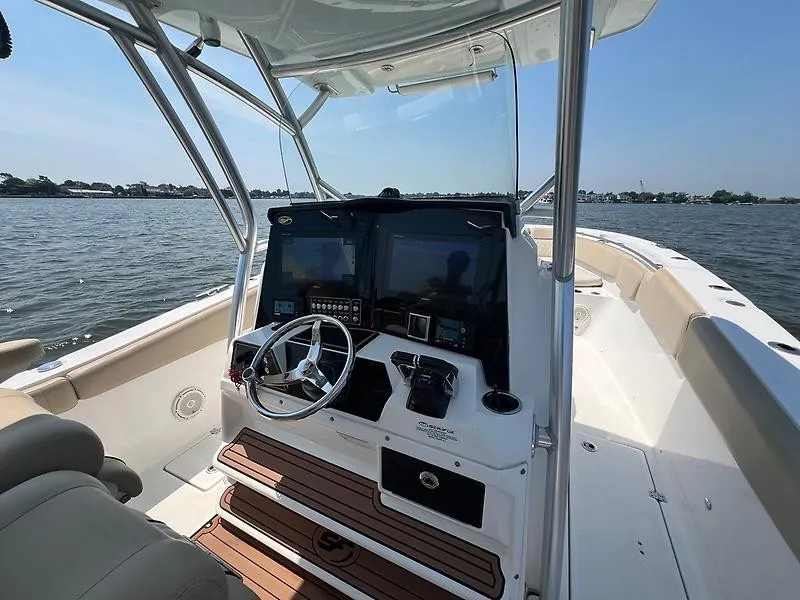 Slide: The Image of The image shows the cockpit of a 2018 Sea Fox 328 Commander. It features a modern helm with dual screens and a stainless steel steering wheel. The background displays calm water and a shoreline. - 14
