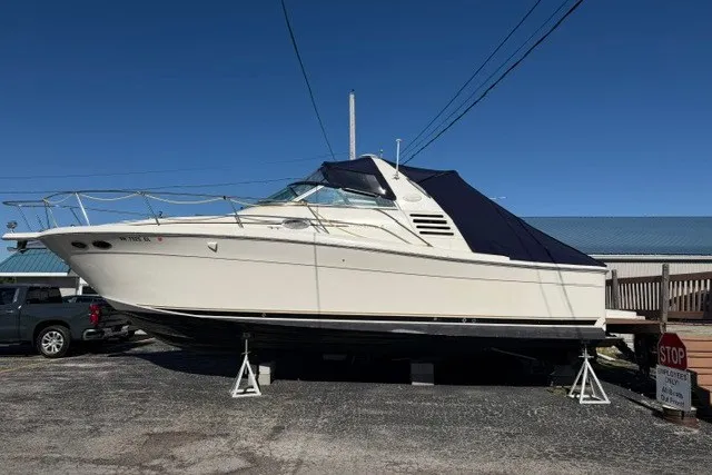 The Image of 1999 Sea Ray 330 Express Cruiser boat on stands, covered, in a parking area. - 0