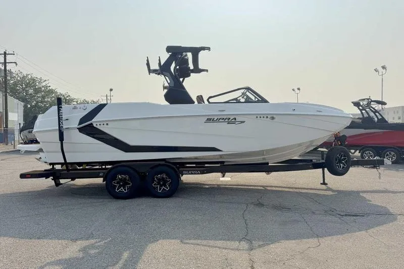 Slide: The Image of 2027 Supra SR boat on trailer, sleek white design, parked outdoors. - 7