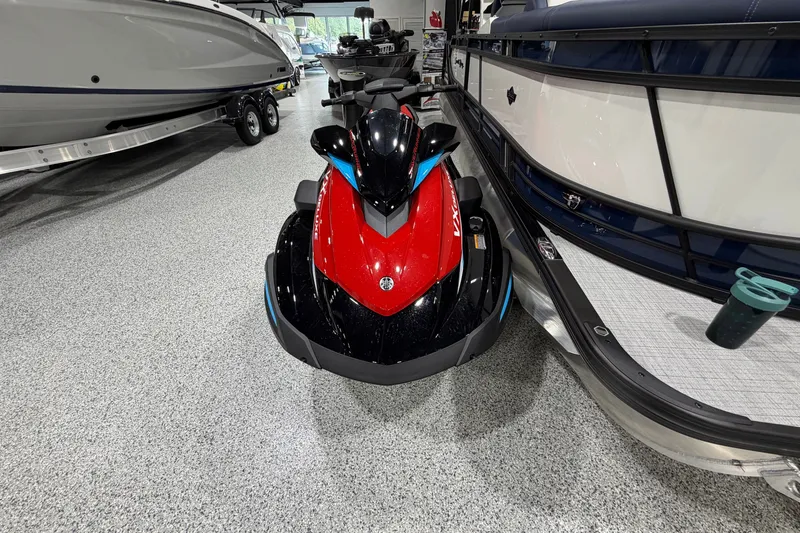 Slide: The Image of 2026 Yamaha WaveRunner VX Deluxe in showroom, red and black design, parked between boats. - 2