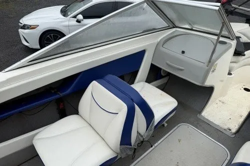Slide: The Image of 2004 Bayliner 194 boat interior with white and blue seating, parked near a white car. - 10