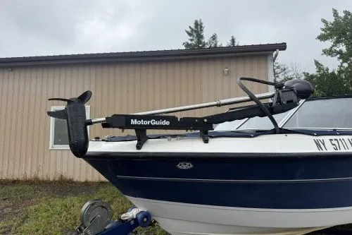 Slide: The Image of 2004 Bayliner 194 boat with MotorGuide trolling motor, parked near a beige building. - 2