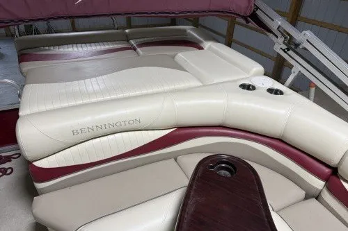 Slide: The Image of 2004 Bennington 2575 boat interior with beige and maroon seating, cup holders, and wood accents. - 3