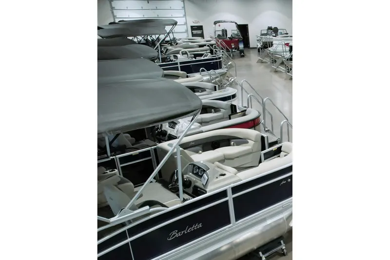 The Image of Several pontoon boats are lined up indoors, featuring black canopies and white seating. - 1