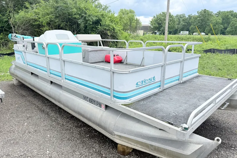 Slide: The Image of 1993 Crest Sport pontoon boat on gravel, surrounded by greenery and cloudy sky. - 1