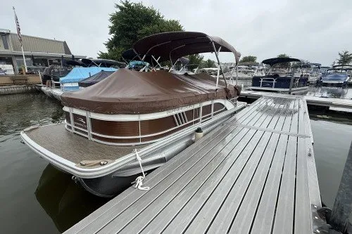 Slide: The Image of 2022 Bennington 22LSR pontoon boat docked with brown cover and canopy. - 2