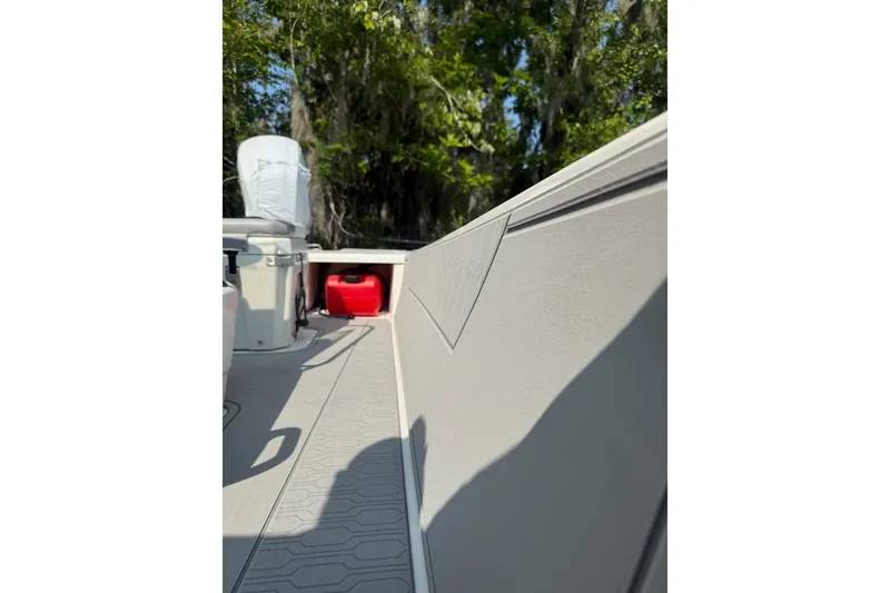 Slide: The Image of 2025 Mako Pro Skiff 17 CC interior with storage and seating, surrounded by lush greenery. - 8