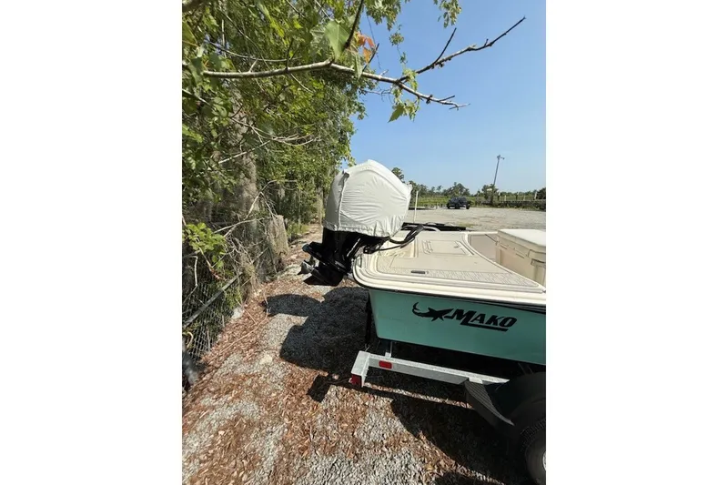 Slide: The Image of 2025 Mako Pro Skiff 17 CC boat parked on gravel near trees. - 14