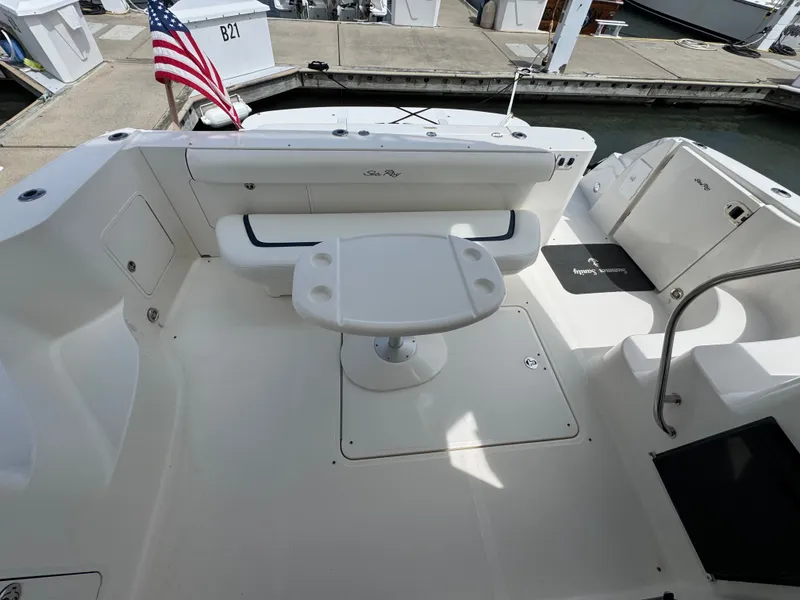 Slide: The Image of The image shows the cockpit of a 2007 Sea Ray 44 Sedan Bridge. There's a bench seat, table, and an American flag. The area is clean and well-maintained, with access to the dock. - 17