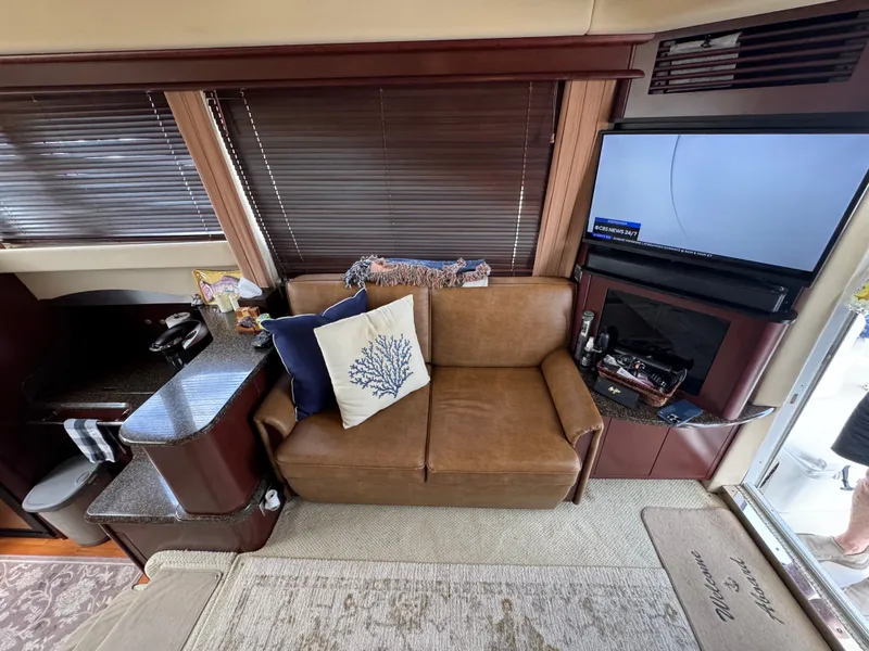 Slide: The Image of The image shows the interior of a 2007 Sea Ray 44 Sedan Bridge. There's a brown sofa with decorative pillows, a TV, and a small kitchenette. - 5