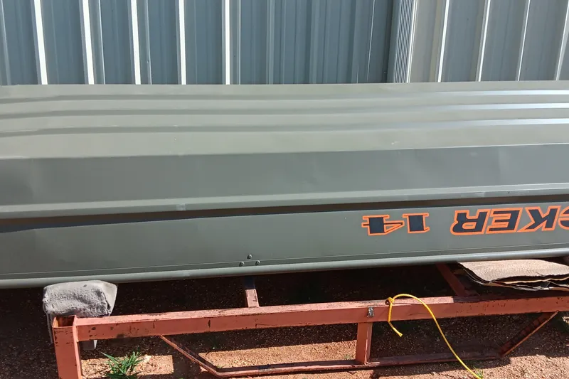 The Image of 2026 Tracker Grizzly 1436 Jon boat on trailer, parked by metal building. - 0