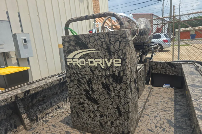 Slide: The Image of Camouflage-patterned Pro Drive 2054 X Series TD CC boat, 2026 model, parked outdoors. - 9