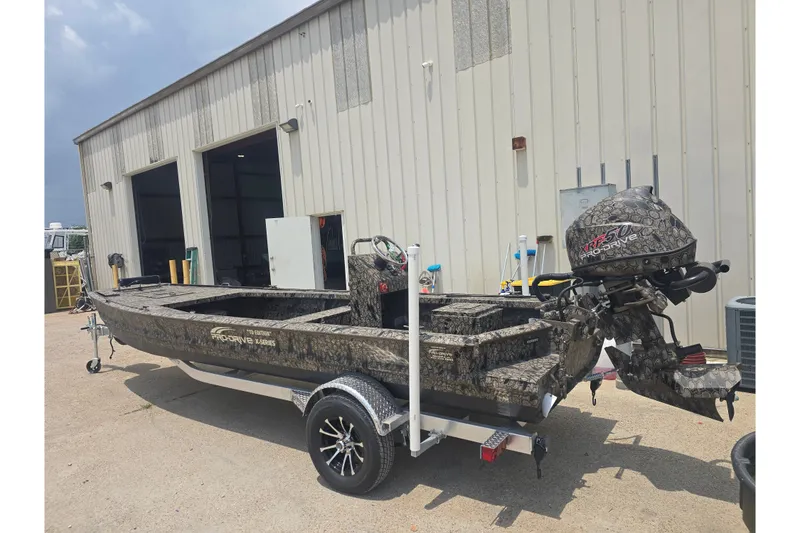 Slide: The Image of 2026 Pro Drive 2054 X Series TD CC boat with camo design, parked outside a building. - 2