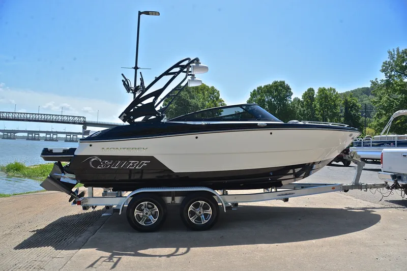 Slide: The Image of 2020 Monterey 218 Surf boat on trailer by riverside with bridge in background. - 15