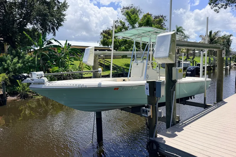 Slide: The Image of 2015 Pathfinder 2300 HPS boat on lift, docked by lush greenery under a partly cloudy sky. - 2