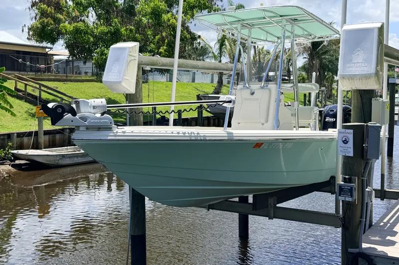Slide: The Image of 2015 Pathfinder 2300 HPS boat on lift, docked by a canal with lush greenery. - 7