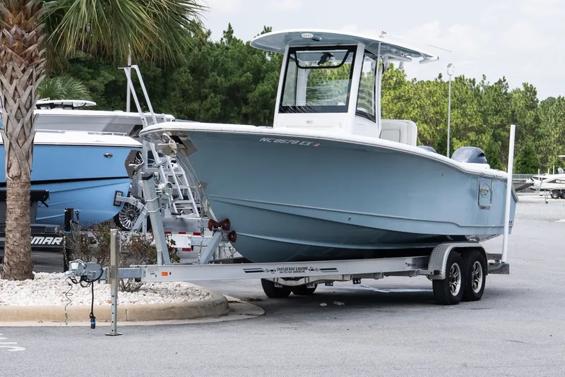 Slide: The Image of 2022 Sea Hunt Ultra 265SE boat on trailer in parking lot, surrounded by trees. - 2