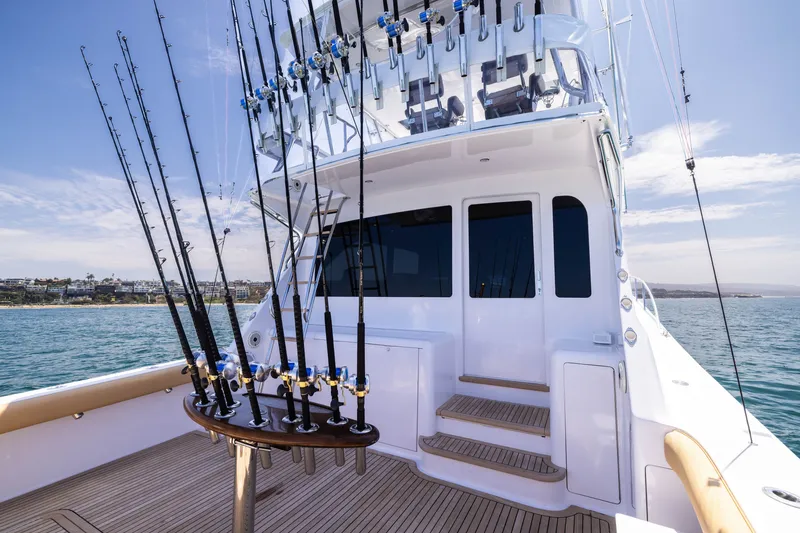 Slide: The Image of 2001 Viking 55 Convertible yacht with fishing rods, docked near a scenic coastline. - 7