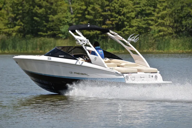 Slide: The Image of 2020 Regal LS2 Surf boat cruising on a lake with lush green background. - 4