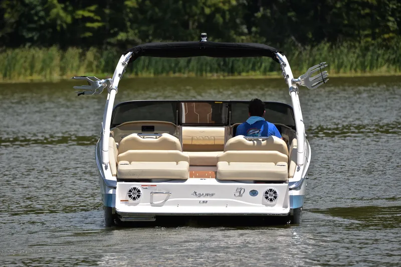 Slide: The Image of 2020 Regal LS2 Surf boat cruising on a calm lake with lush greenery. - 9