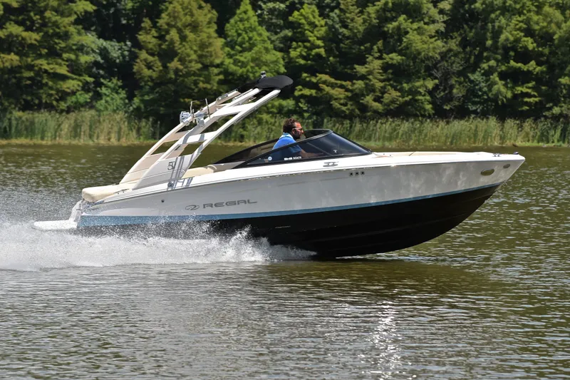 Slide: The Image of 2020 Regal LS2 Surf boat cruising on a lake with lush green trees. - 3