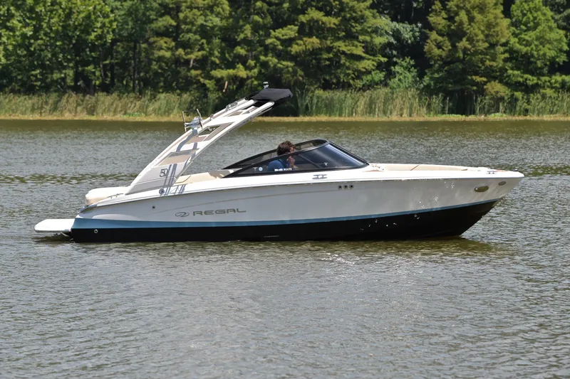 Slide: The Image of 2020 Regal LS2 Surf boat cruising on a serene lake with lush greenery. - 8