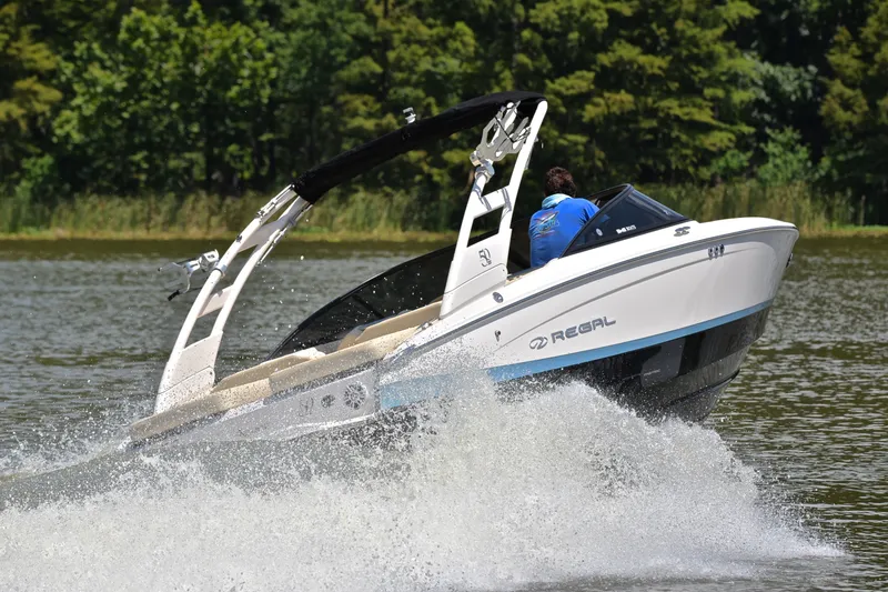 Slide: The Image of 2020 Regal LS2 Surf boat speeding on a lake with lush green trees in the background. - 5