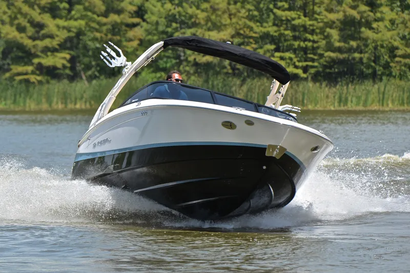 Slide: The Image of 2020 Regal LS2 Surf boat cruising on a lake with lush greenery in the background. - 7